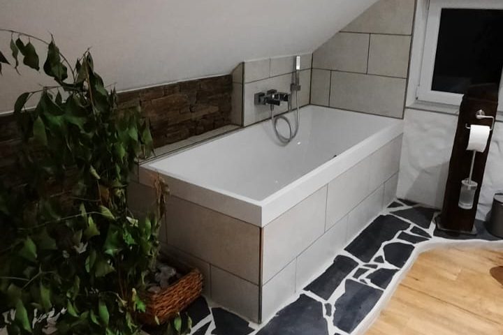 Badewanne in einem schlichten Badezimmer mit Pflanze und Holzdetails.