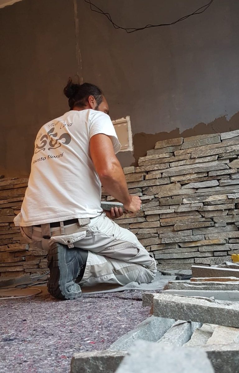 Handwerker verlegt Steinplatten an einer Wand, kniend auf dem Boden.