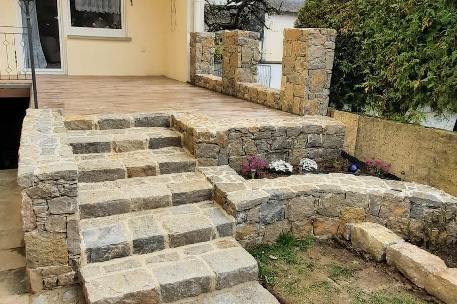 Muschelkalktreppe und Terrasse aus Keramikplatten mit bepflanztem Bereich und angrenzendem Garten.