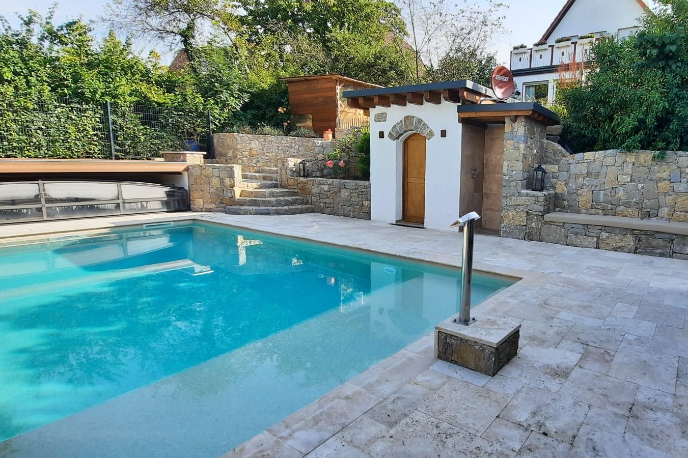 Ein klarer Swimmingpool umgeben von Steinterrassen und üppigem Grün.