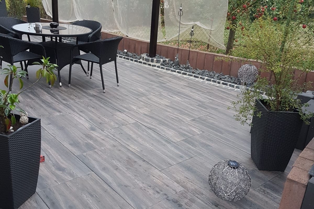 Terrasse mit Tisch, Stühlen und Pflanzen in Töpfen auf grauem Boden.