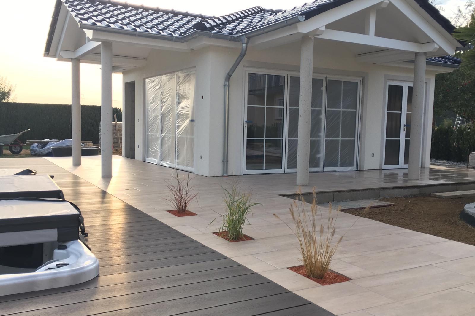 Modernes Haus mit Veranda, weißen Wänden und kleinen Pflanzen in roten Töpfen.