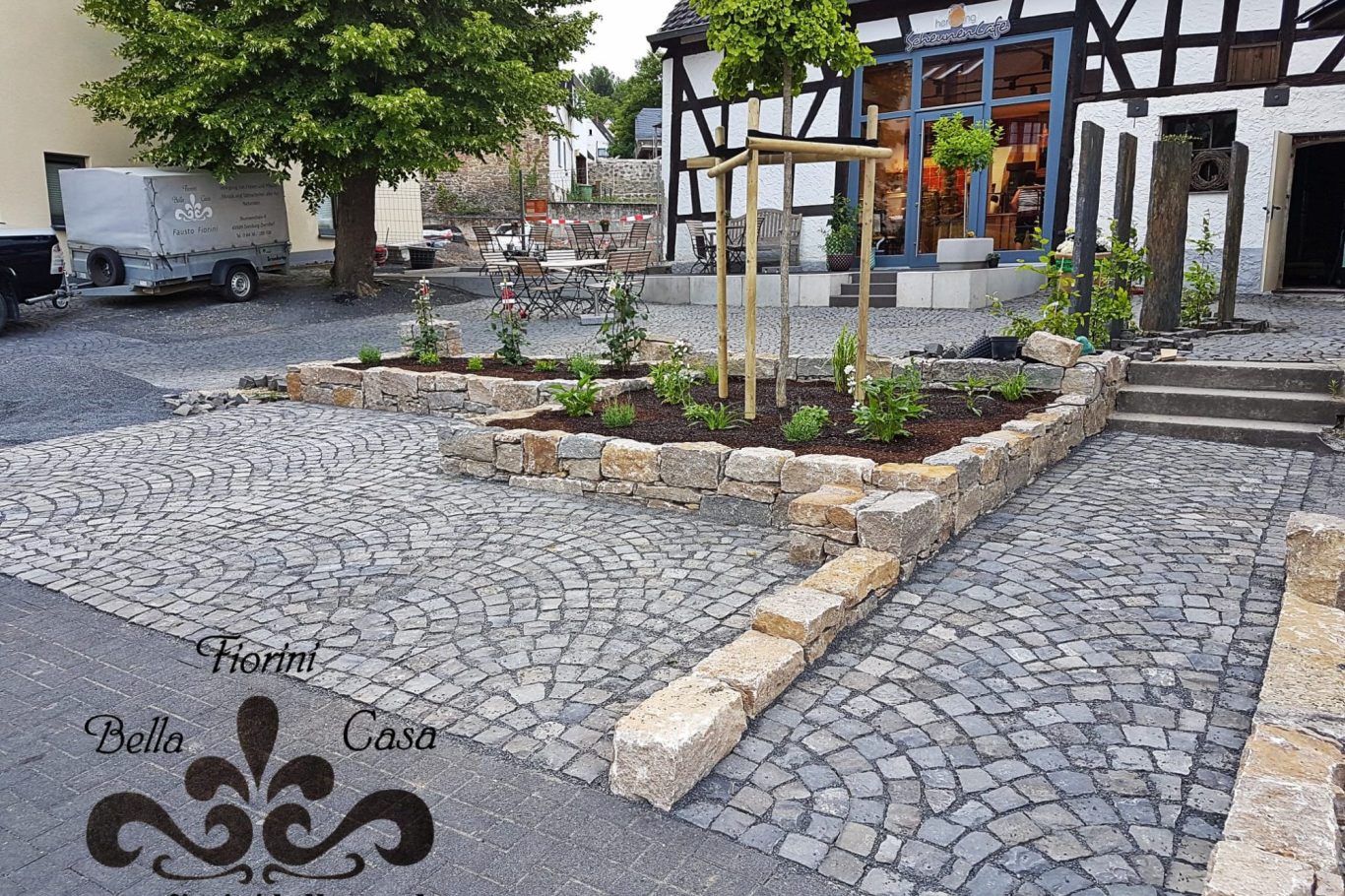 Steinerne Einfassung mit Pflanzenbeet und gepflastertem Platz in ländlicher Umgebung.