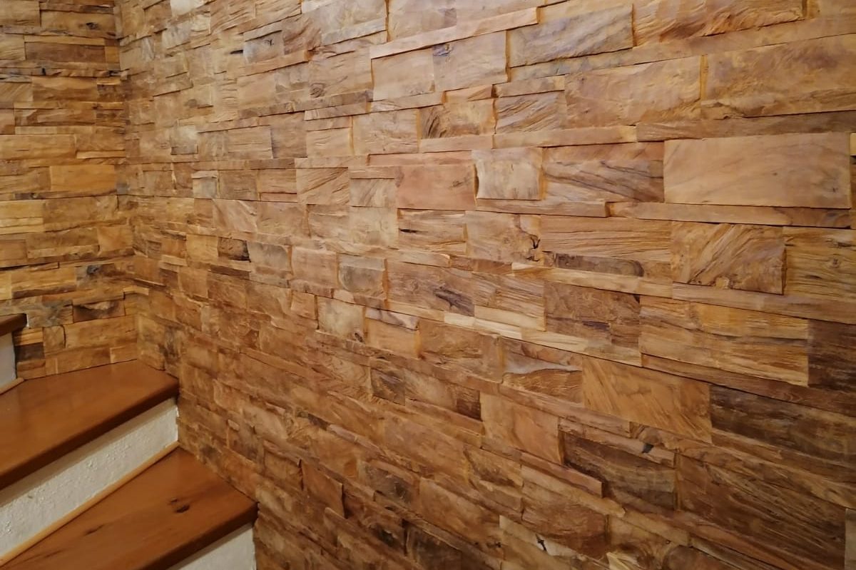 Holzwand mit strukturierten Natursteinen und einer Holztreppe im Vordergrund.