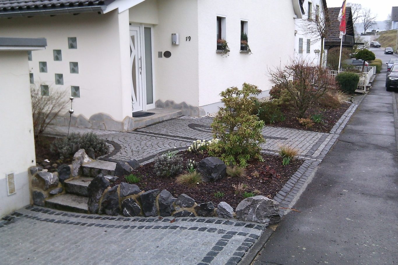 Eingangsbereich eines Hauses mit Steinen, Pflanzen und einem Gehweg.