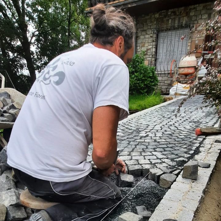 Mann verlegt Natursteinpflaster vor einem Haus im Freien.